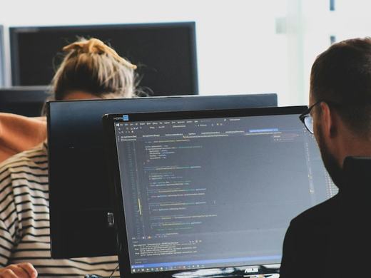Duas pessoas programando em frente a monitores com código na tela